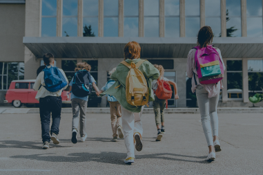 Children wearing backpacks skip and run into a school building 